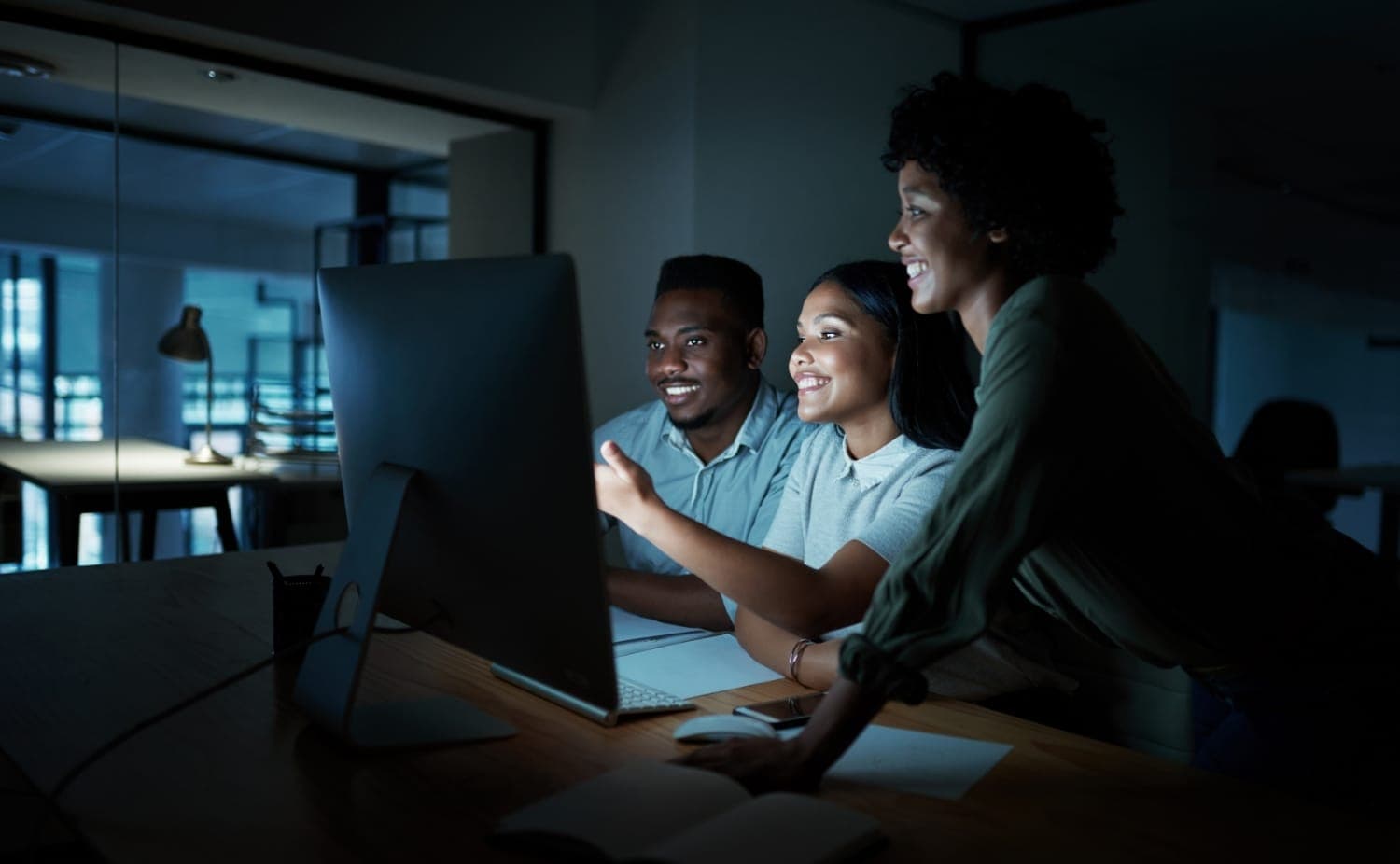 Three colleagues looking at the same screen together, late in an office