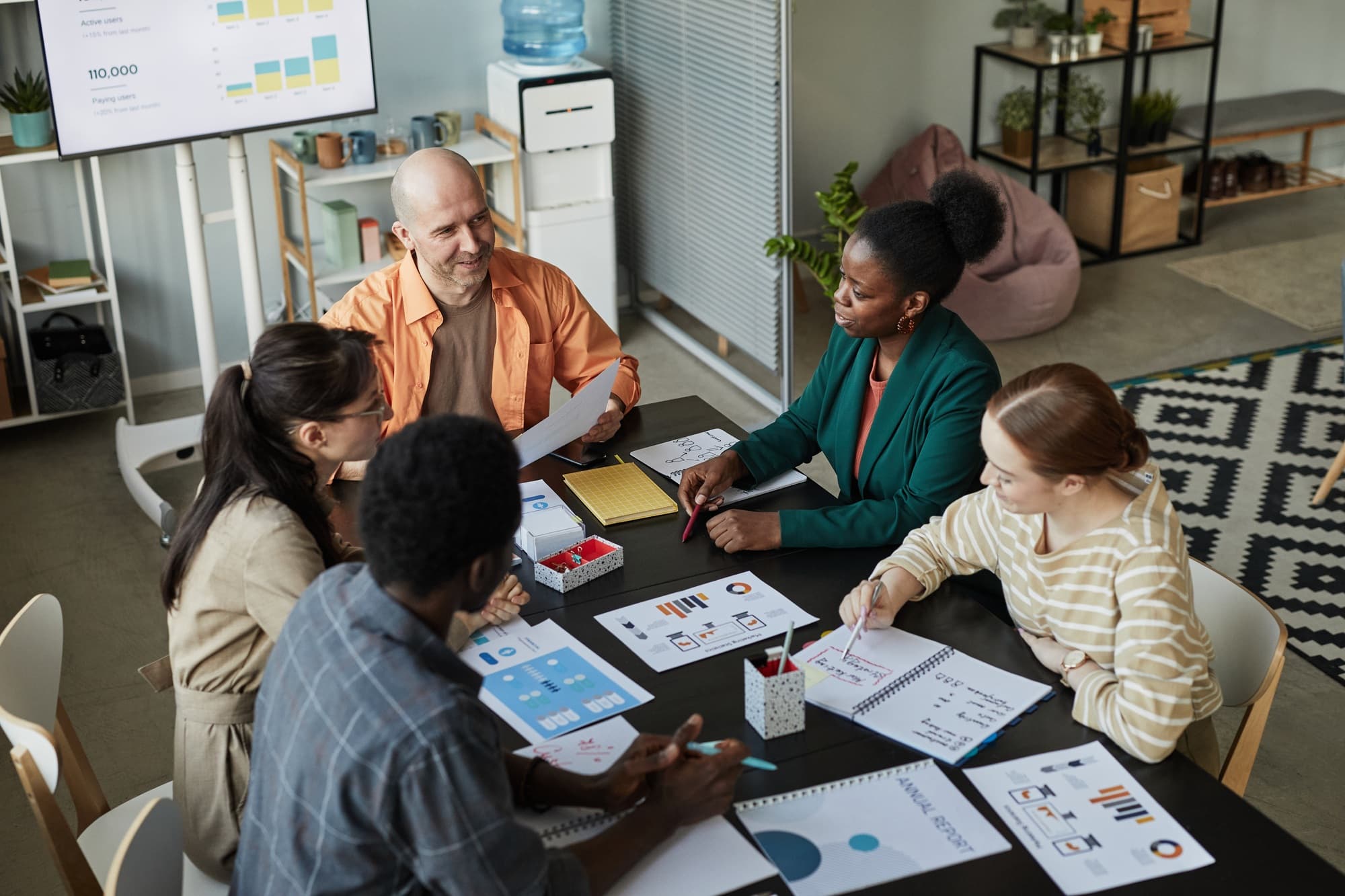 A mixed team in a meeting, laptops and notes across the table