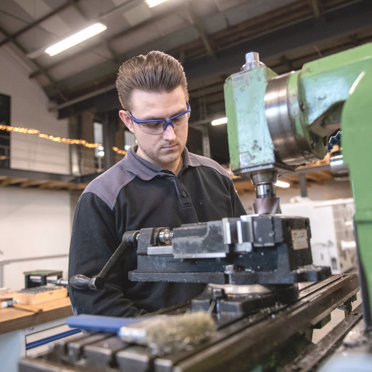 An engineer in safety glasses working at a machine on the shop floor